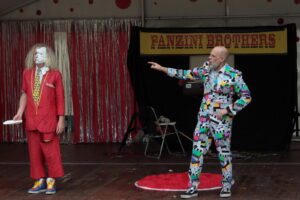 Man in colourful suit pointing at man in red with cream pie on one side of his face