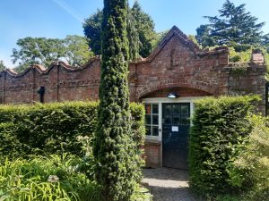 Red brick arts & crafts building behind yew hedges