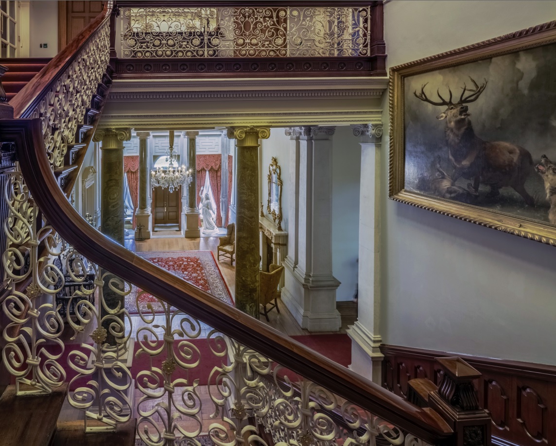 View over banisters of Farmleigh entrance hall featuring painting of stag, Connemara marble pillars, red Persian rug and Carrara marble statue