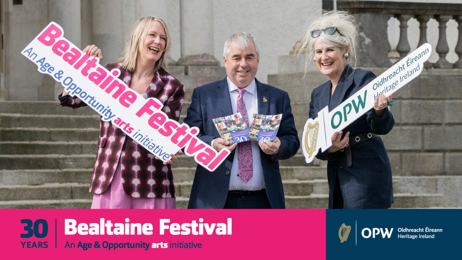 two women and a man in front of steps into historic building holding signs for Bealtaine festival