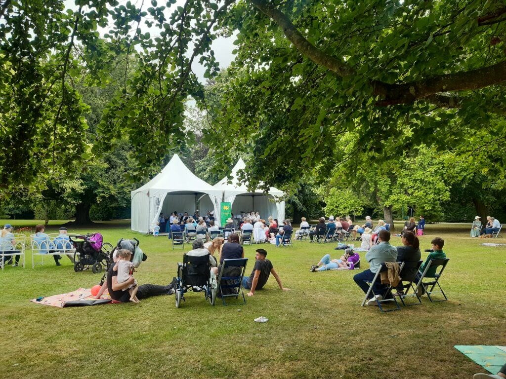 People on lawn watching Brass Band perform in white tent